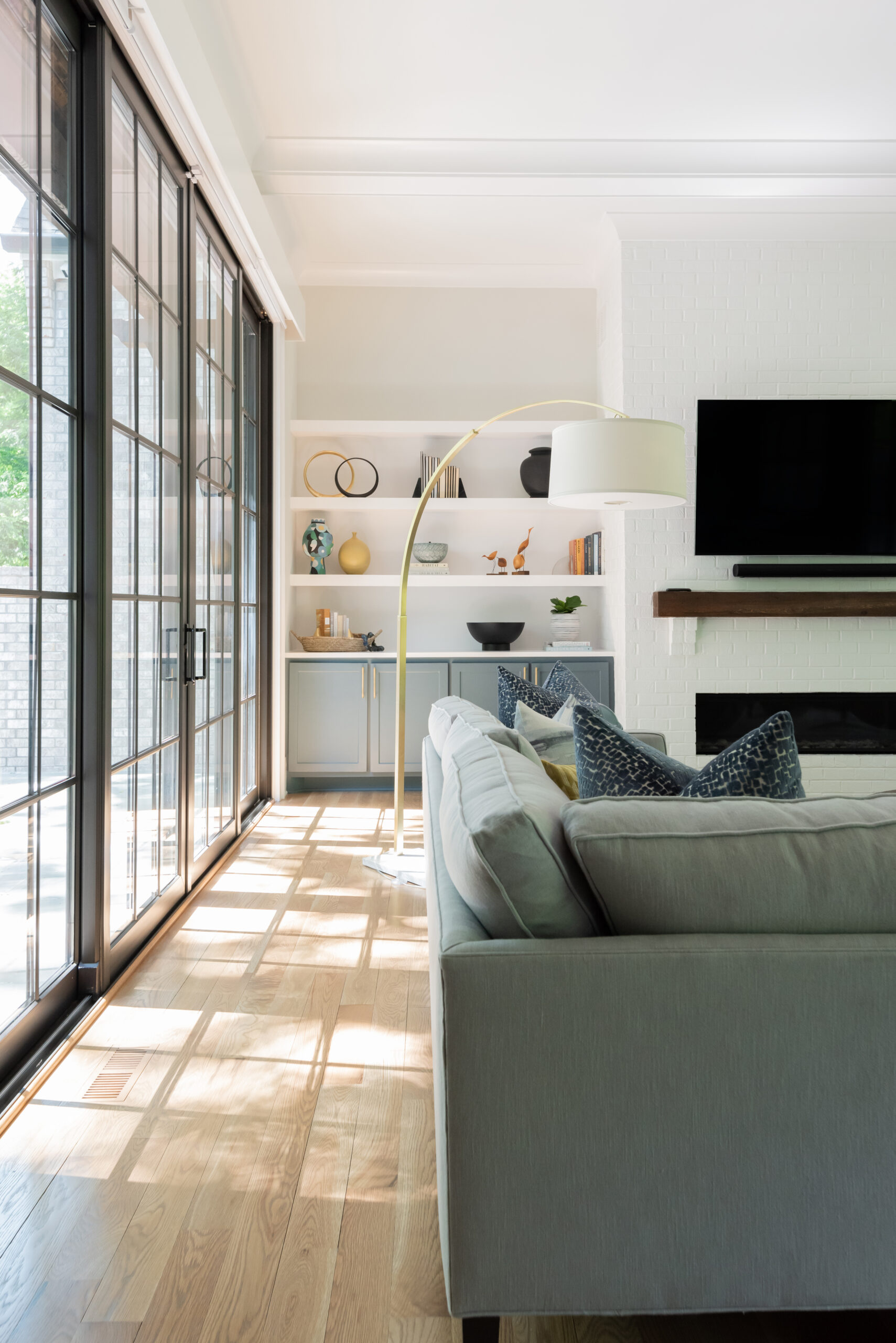 Floor to ceiling black grid window with view of built-in shelving and a partial view of mantle and tv