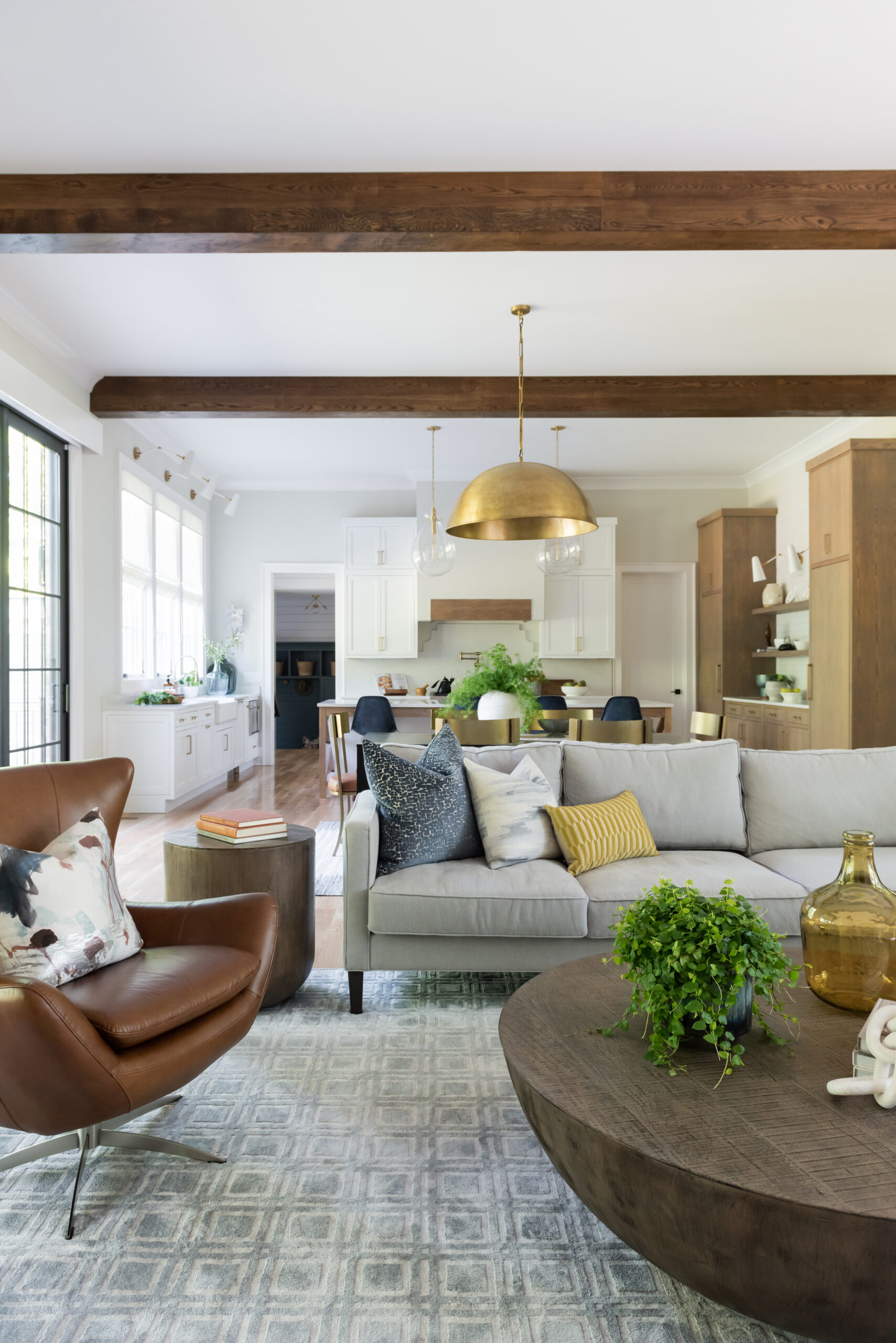 Family room view leading into dining area and kitchen with stained wood ceiling beams and a gold dome chandelier over dining table