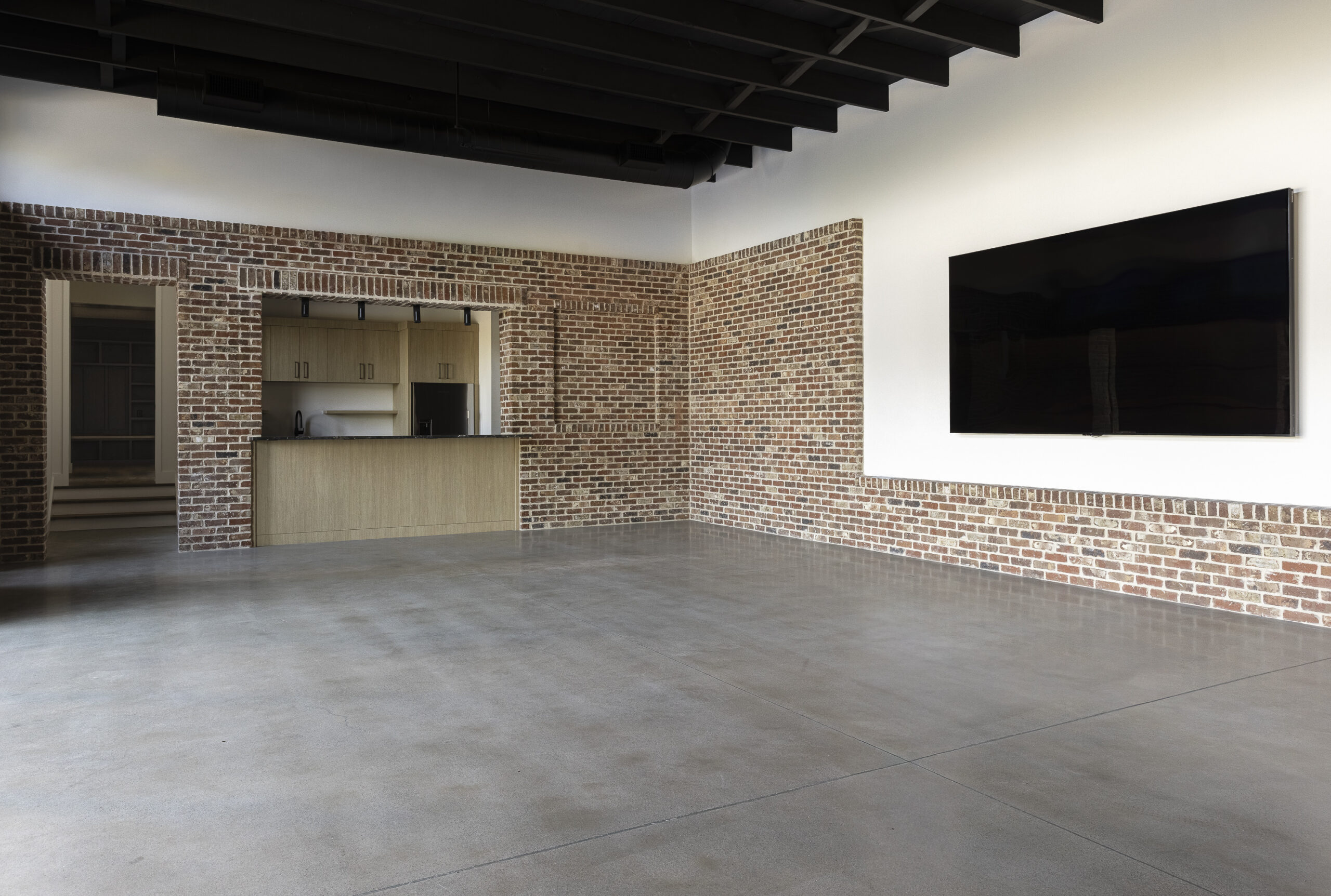 Media room with interior brick walls, black painted exposed beam ceiling and kitchen area along the side