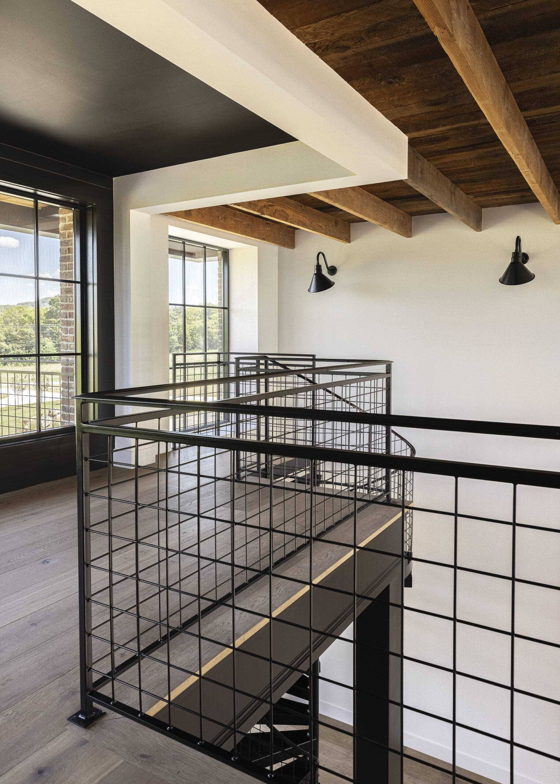 Second floor loft with black iron railing and exposed stained wood beam ceiling