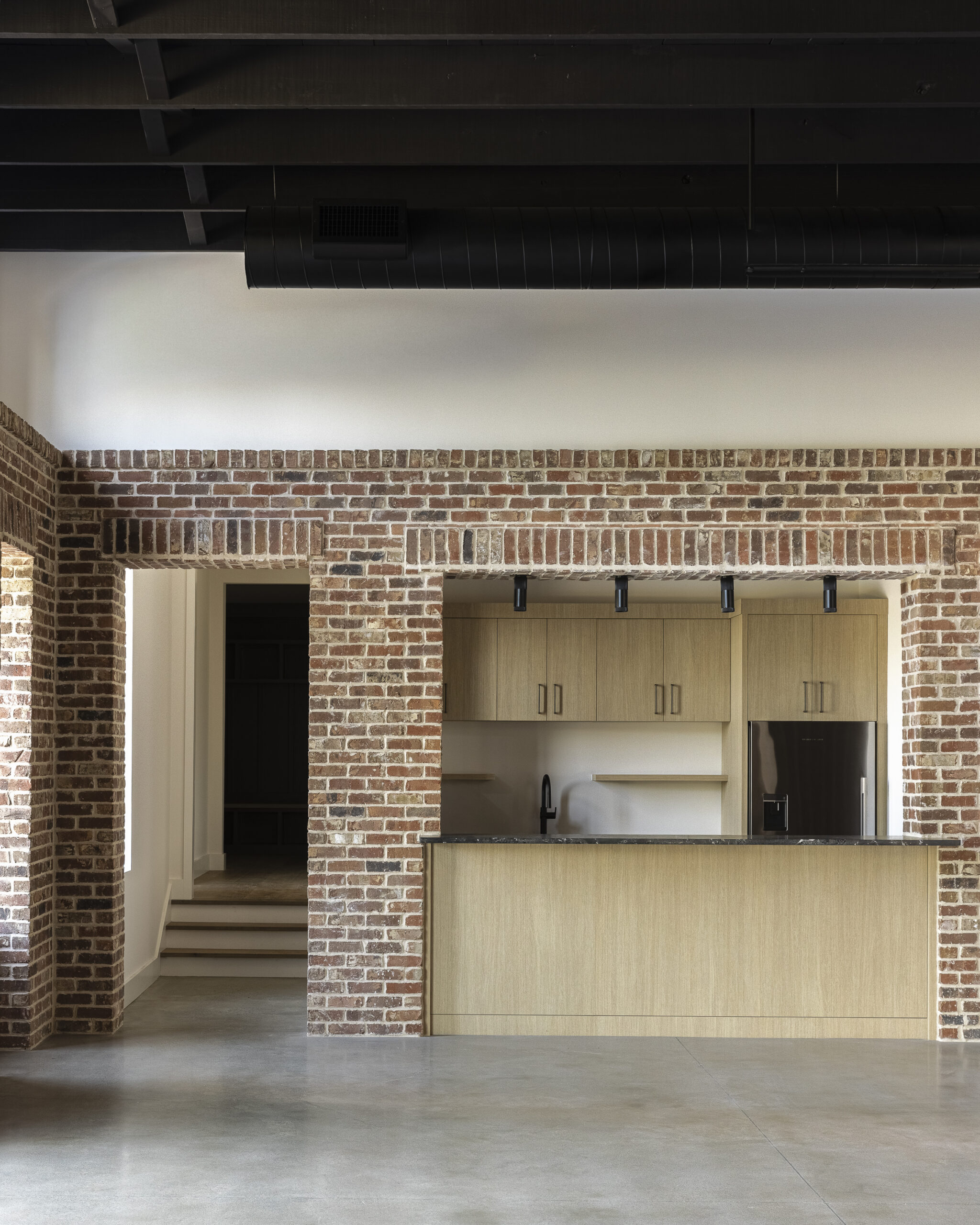 Media room with interior brick walls, black painted exposed beam ceiling and kitchen area along the side