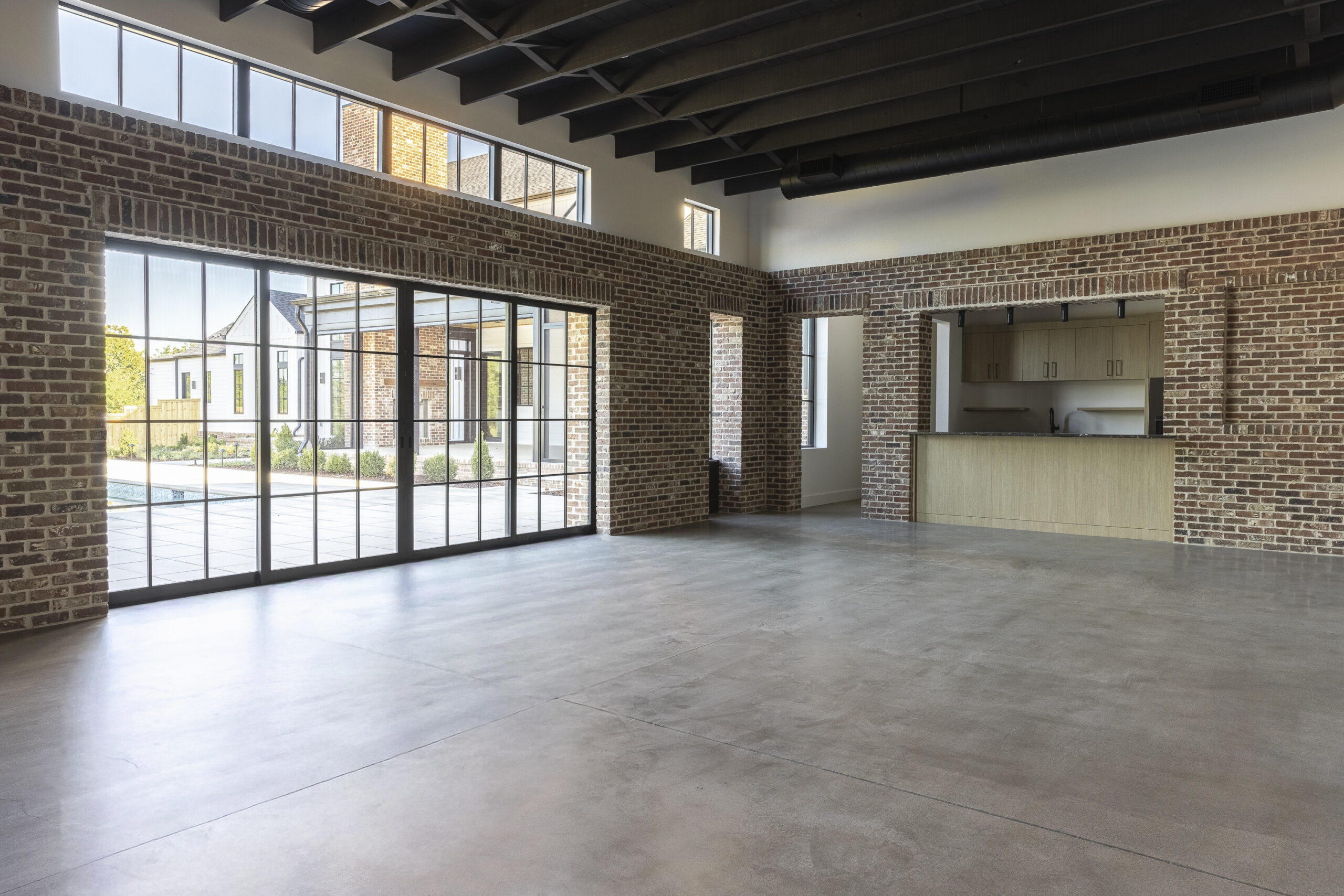 Media room with interior brick walls and large glass doorway overlooking a rectangular pool and a kitchen area along the side
