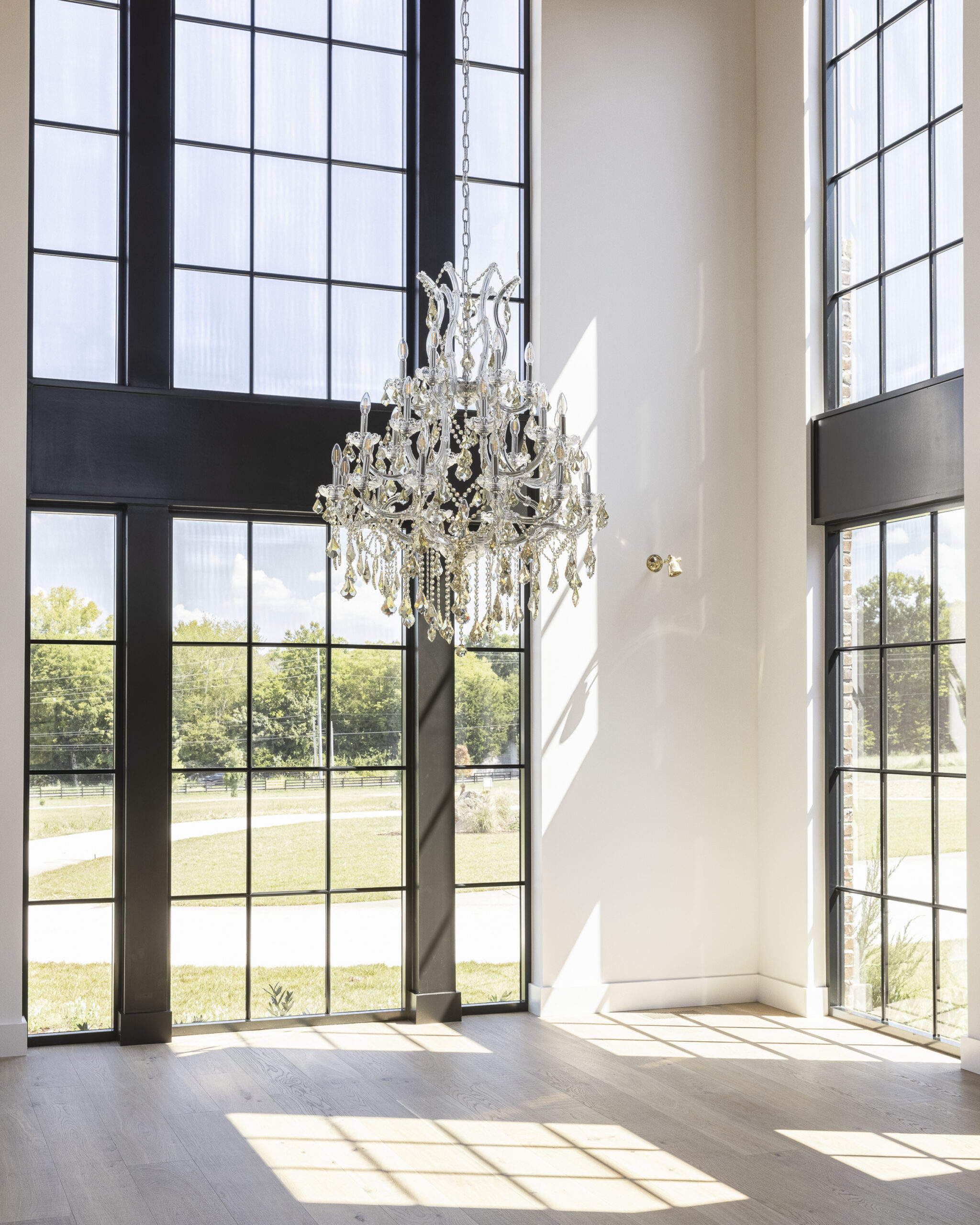 Large floor to ceiling two story windows with black grids and a large crystal chandelier