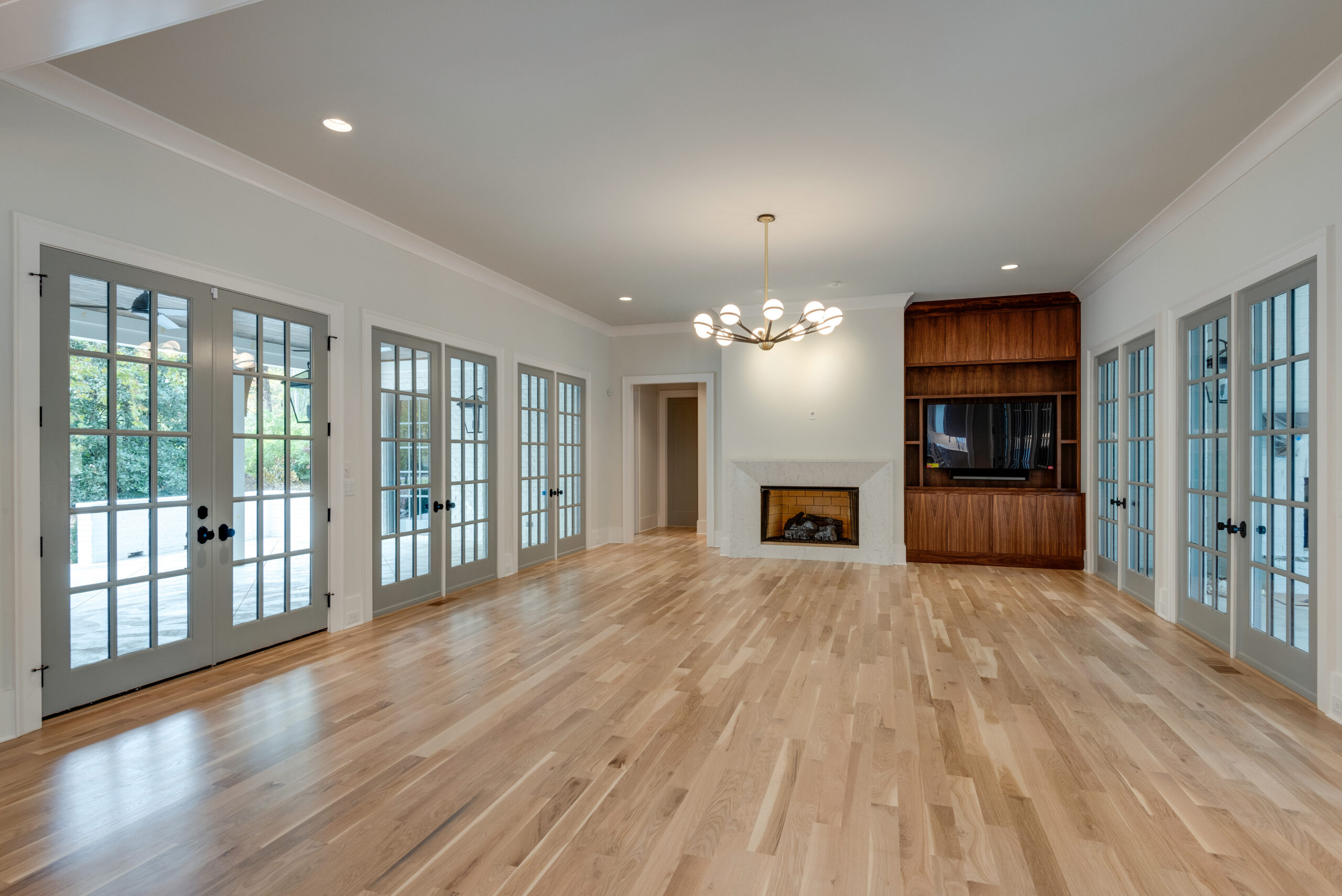 Family room with large grid windows, a fireplace, a circular chandelier, and sleek stained wood paneling behind the tv