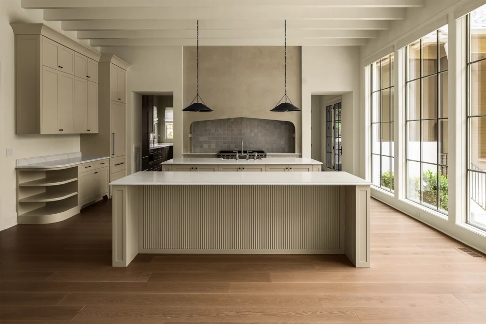 Kitchen with fluted island, black pendant lights, plaster range hood, and a wall of windows