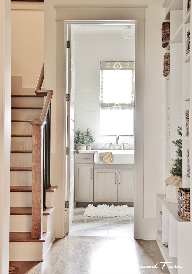 Transition space wit white walls leading into a creamy, neutral laundry room taupe and white diagonal striped tile with stairs and mudbench framing the doorway