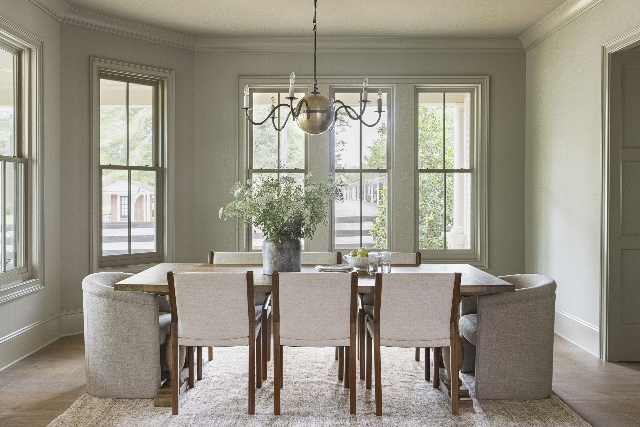 Muted green walls with windows, a chandelier, and table with chairs