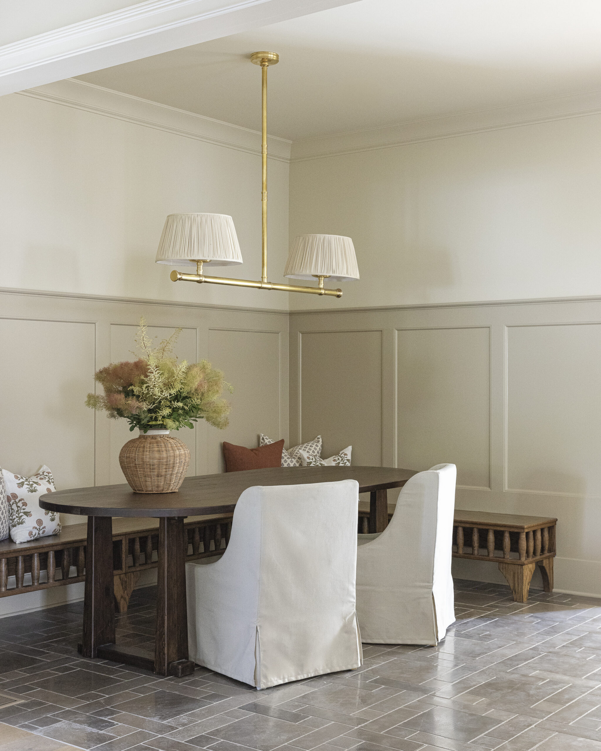 Cream painted walls with taupe paneling, a built-in dark wood stained bench, table with chairs, and a chandelier