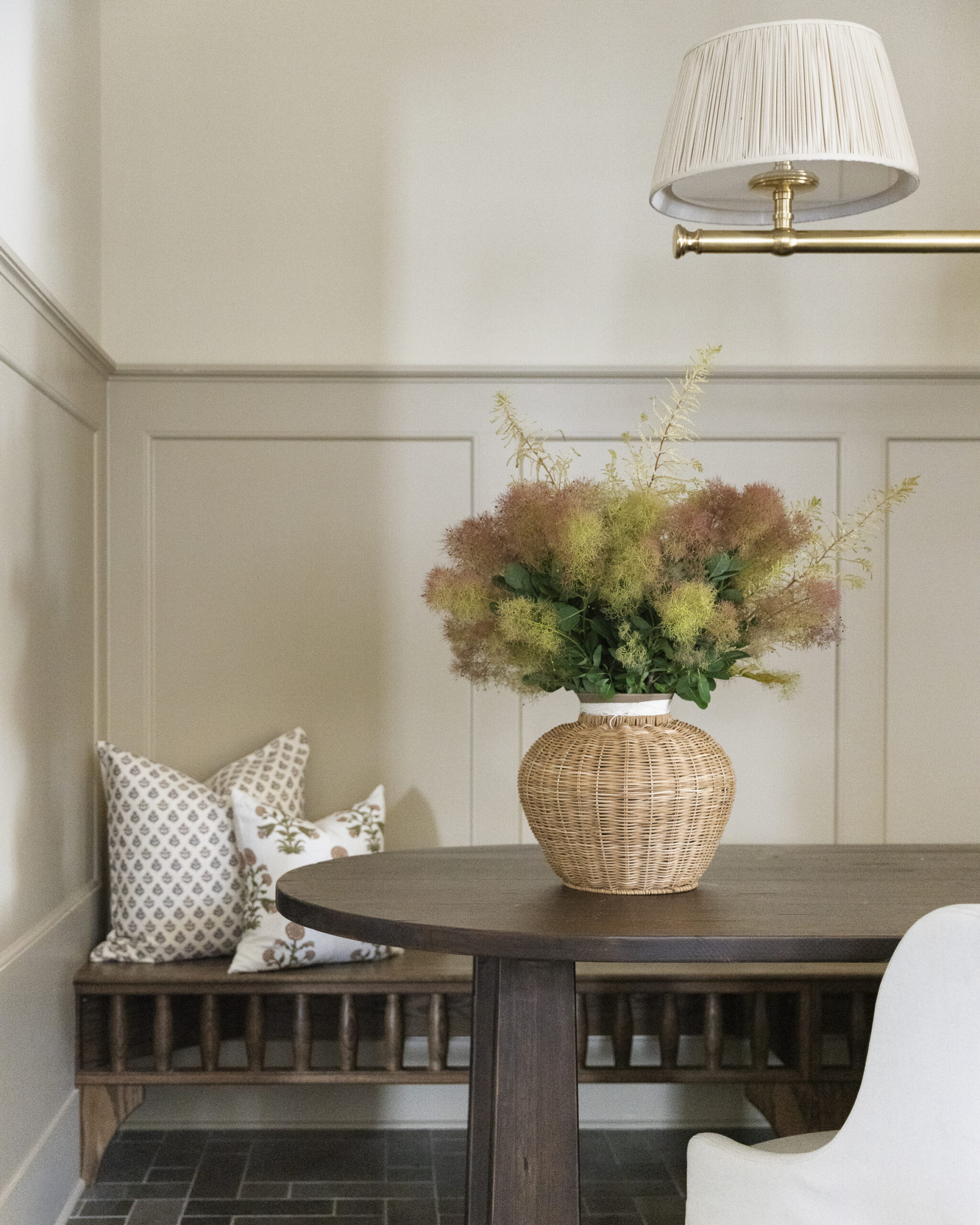 Cream painted walls with taupe paneling, a built-in dark wood stained bench, table with chairs, and a chandelier