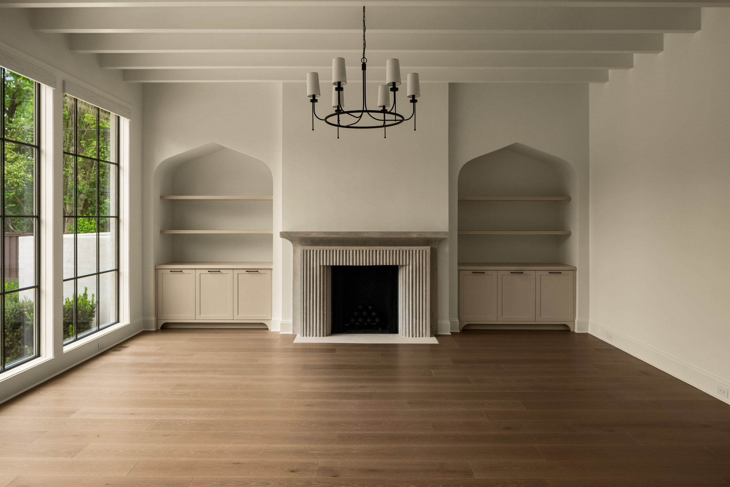 Creamy white walls with centered fireplace flanked with venetian builtin cabinetry with open shelving, a ceiling with painted wood beams and a circular black iron chandelier