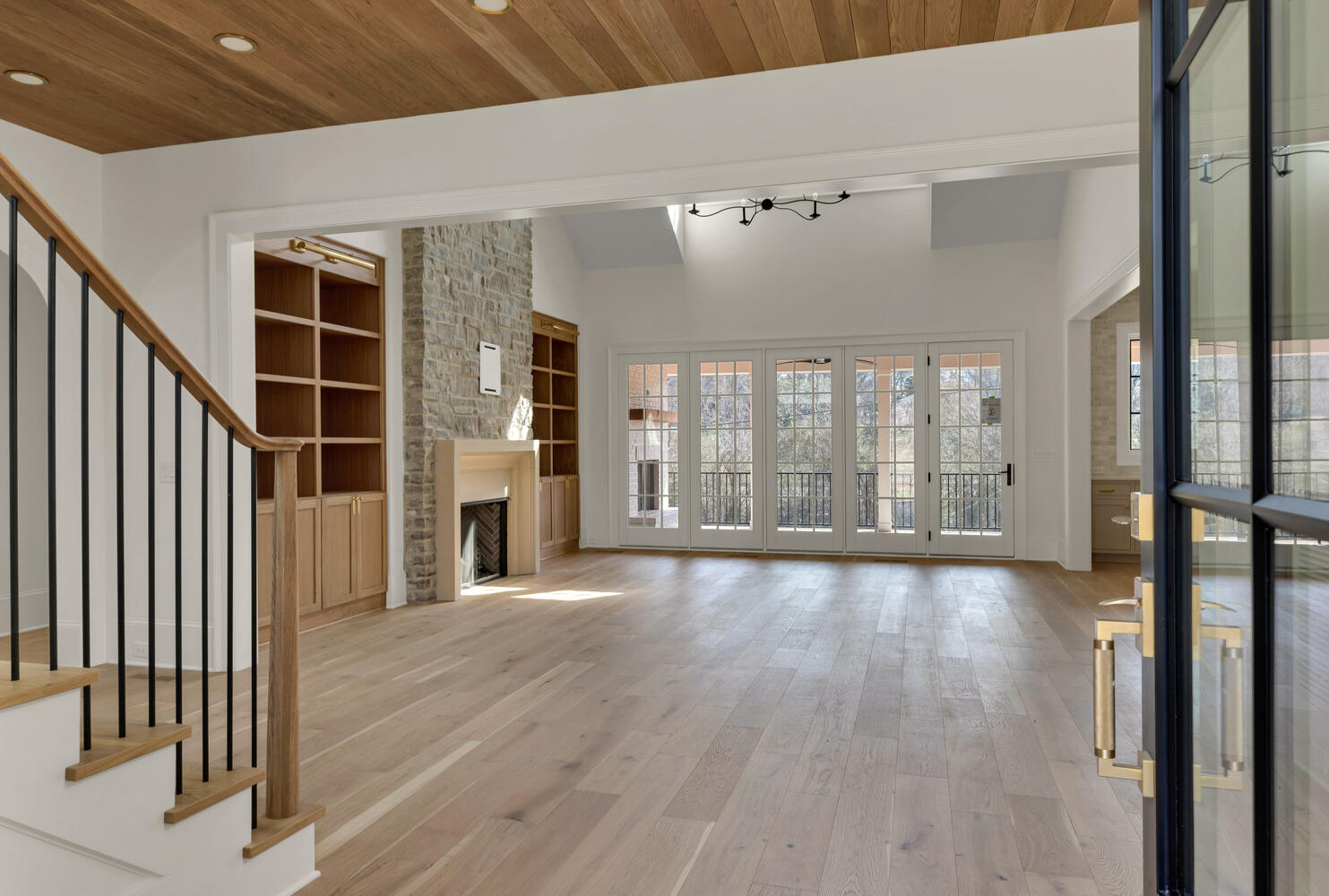 Family room with wall of windows and natural wood stained built-in shelving and stone covered fireplace