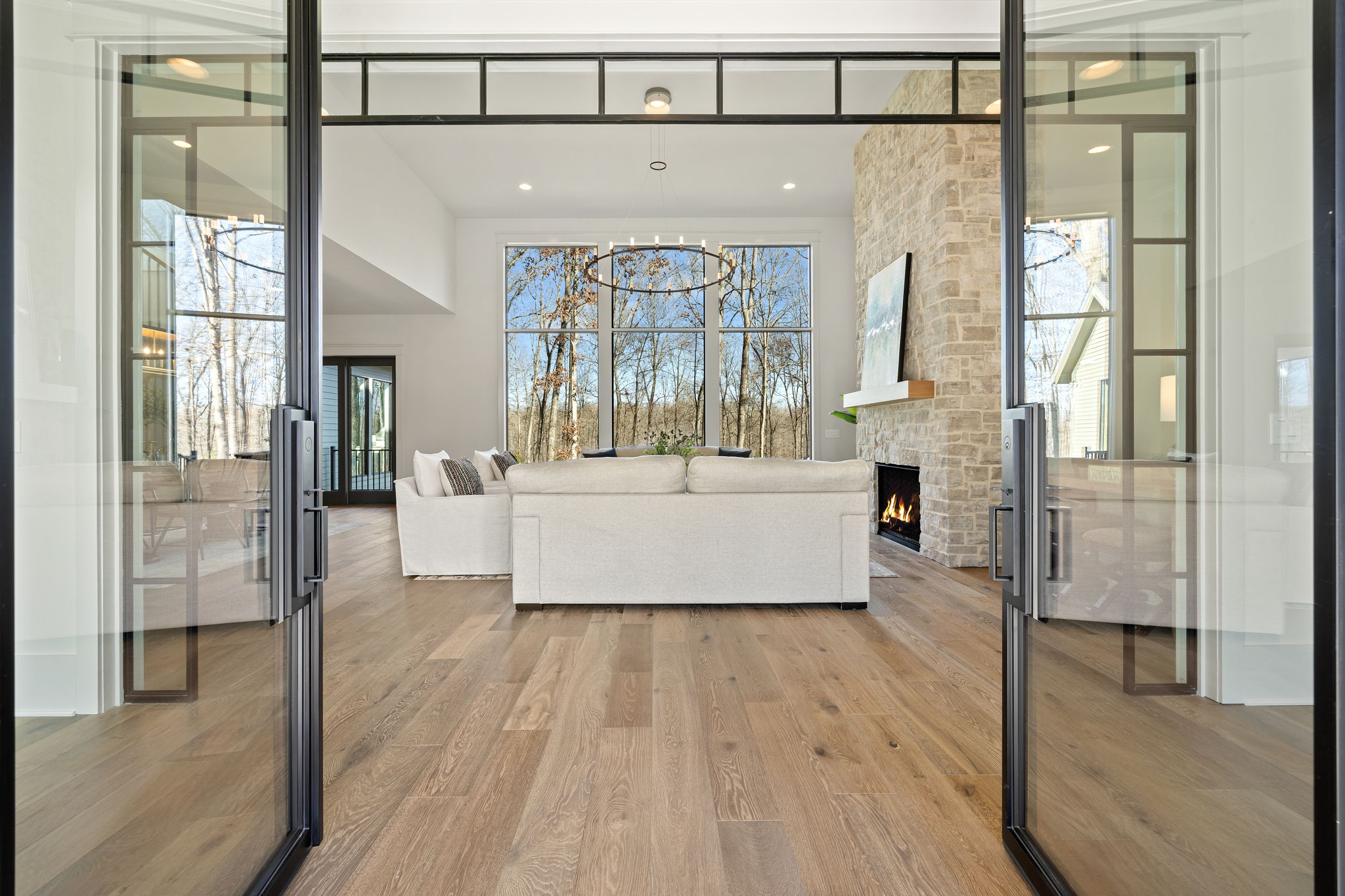 Entryway view of family room with floor to ceiling stone fireplace and large, floor-to-ceiling black grid windows
