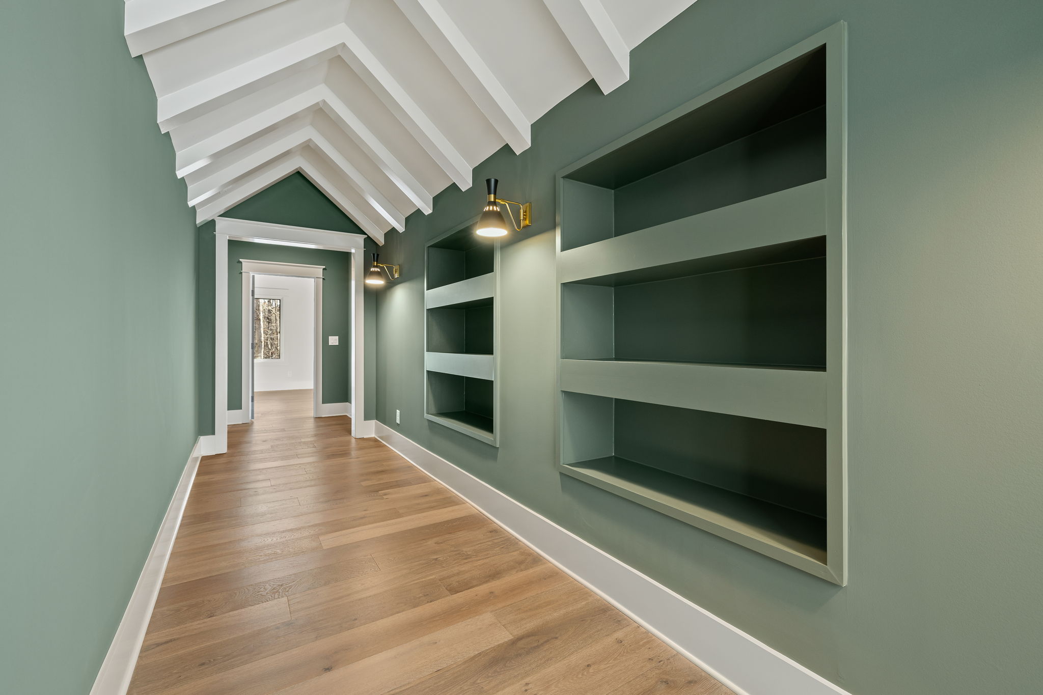 Hallway with green walls and open shelving with sconces and white beams on ceiling