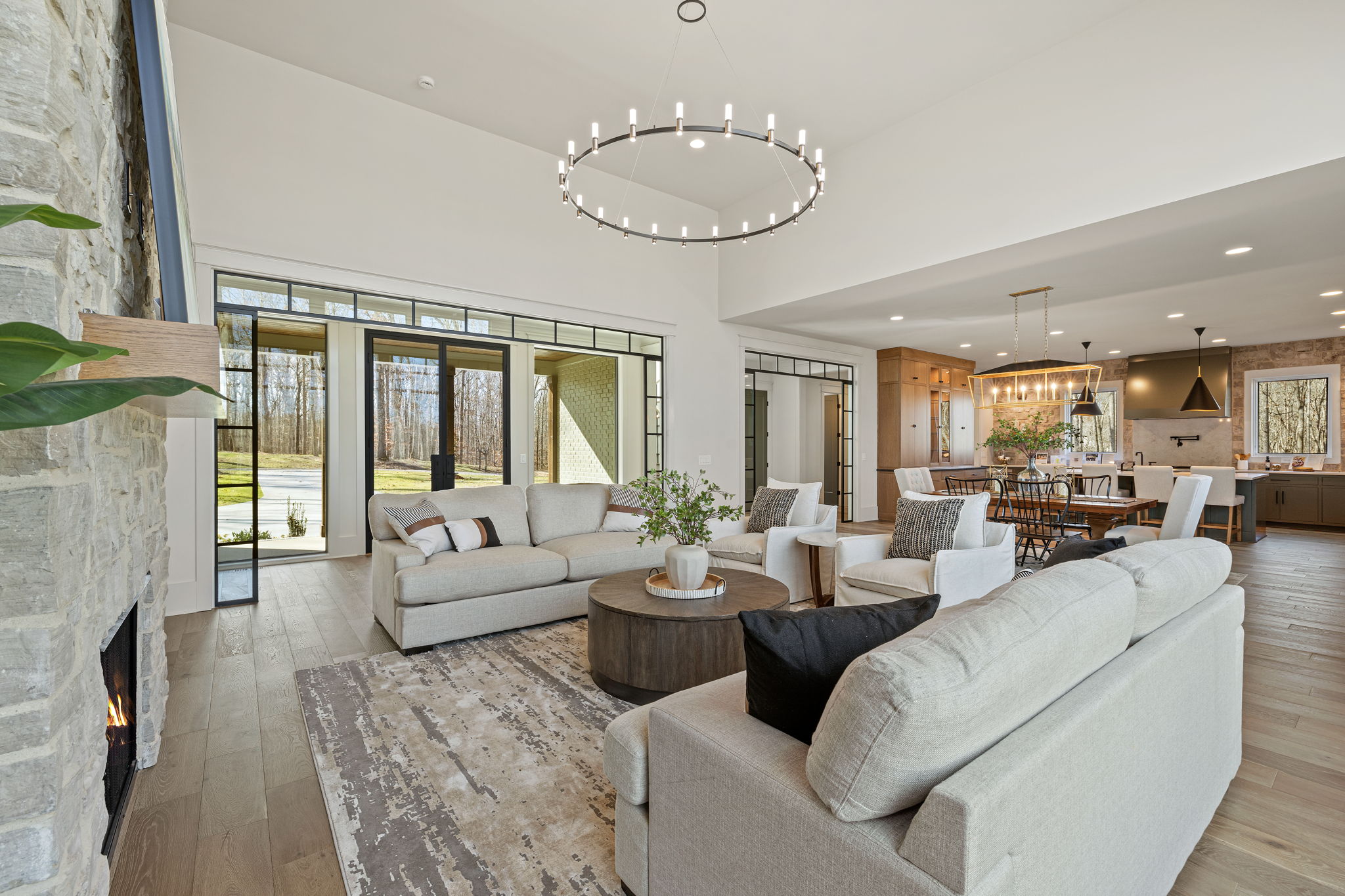 Family room with high ceilings, a circular chandelier, neutral couches, and view of glass front entryway and kitchen