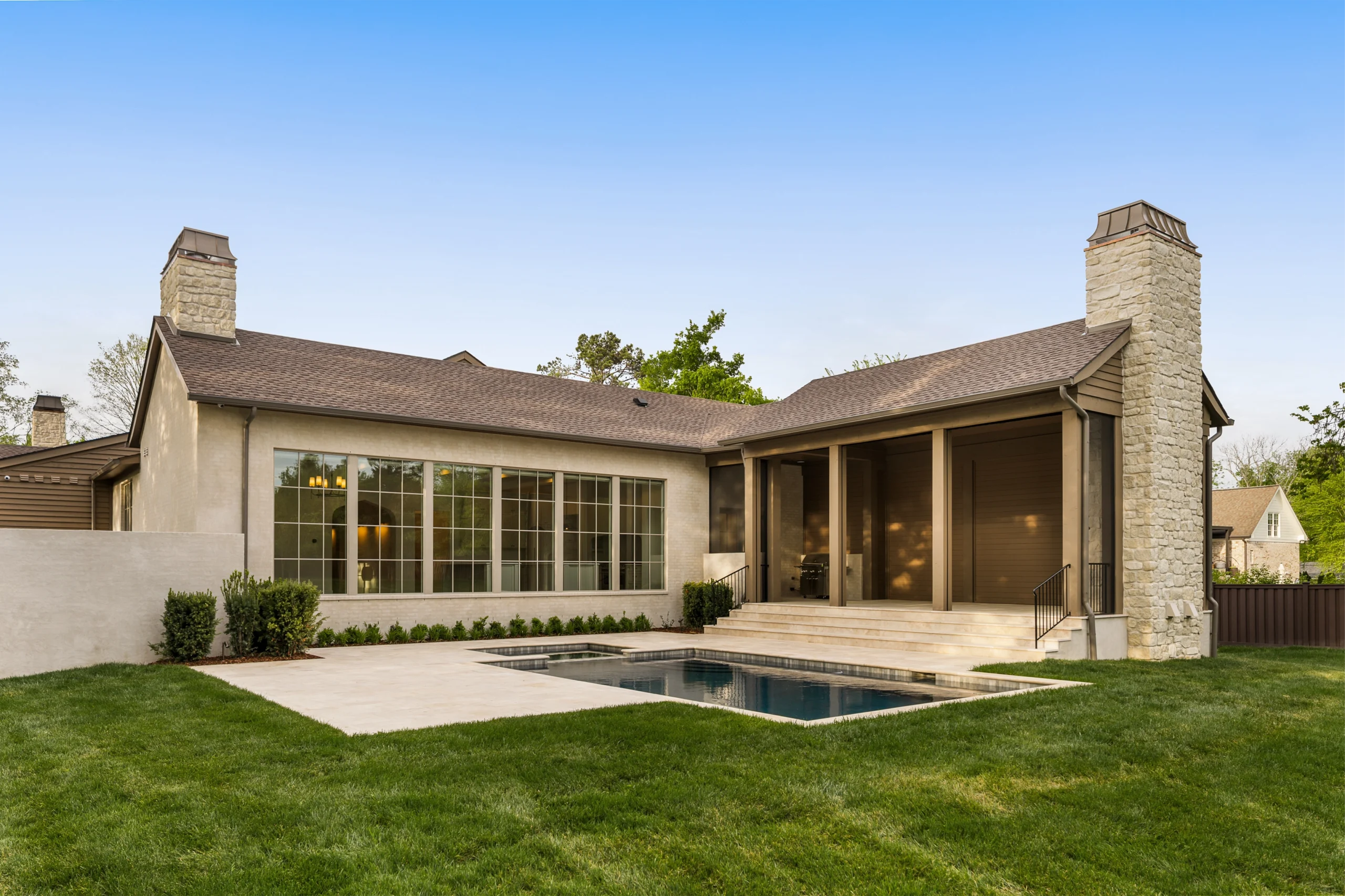 Backyard with in-ground pool and patio with columns connected to a home with a wall of windows