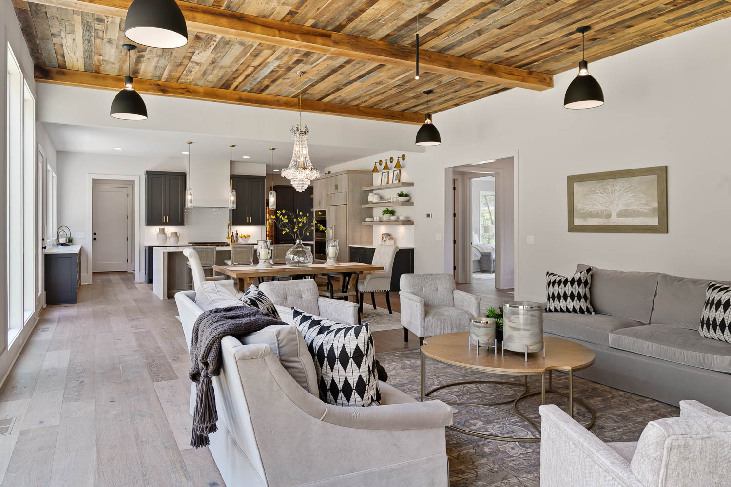 Open floor plan of family room leading into the kitchen with stained, wood paneled ceiling with industrial black spaced lights