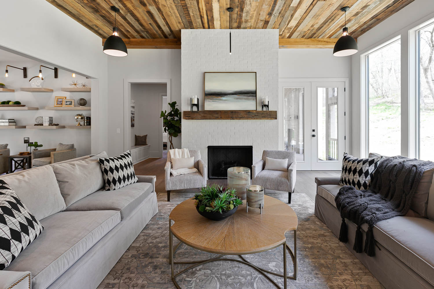 Open floor plan of family room leading into the kitchen with stained, wood paneled ceiling with industrial black spaced lights