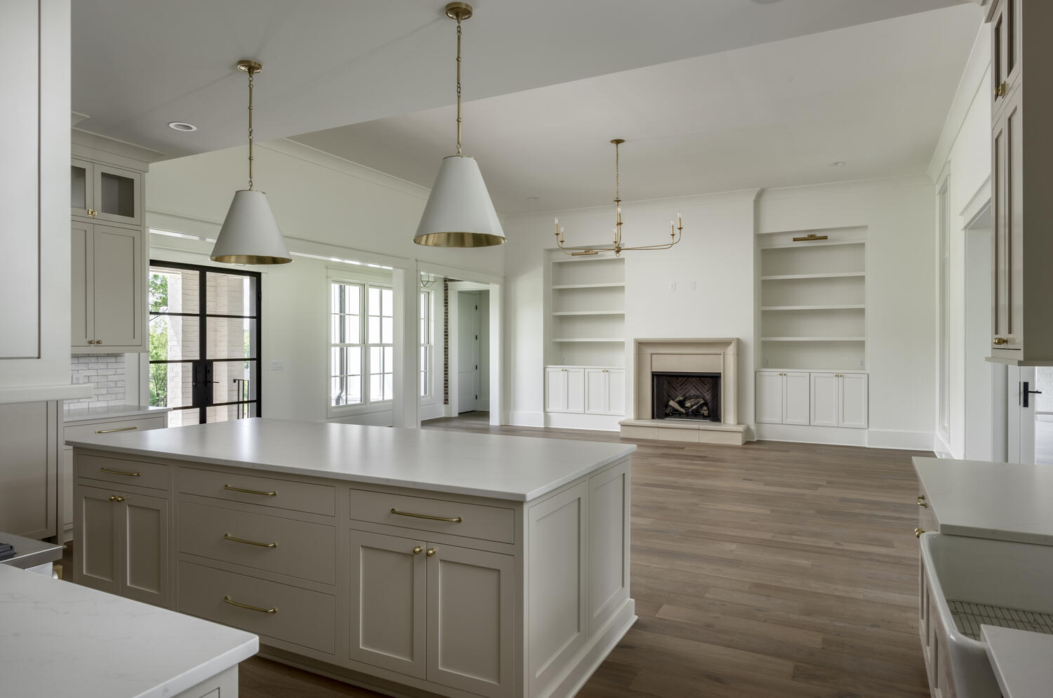 Neutral toned kitchen island with white conical pendant lights with a view of the family room with fireplace and open shelving