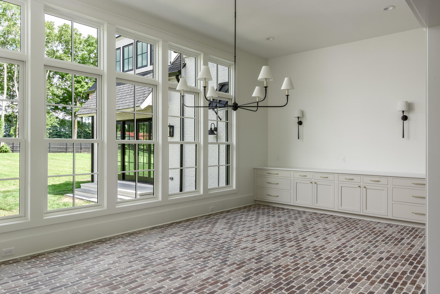 Dining room with red brick flooring, a black iron chandelier, and large, black grid windows
