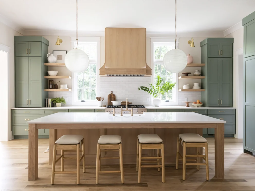 Green kitchen with wood range hood and island, open shelving, globe pendants, and wood counter stools