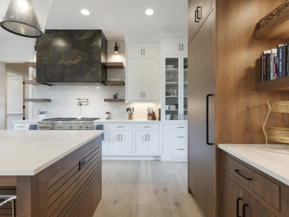 Bright, inviting modern kitchen with white cabinetry, wood island and pantry, marble counters, open shelving, and stainless-steel range