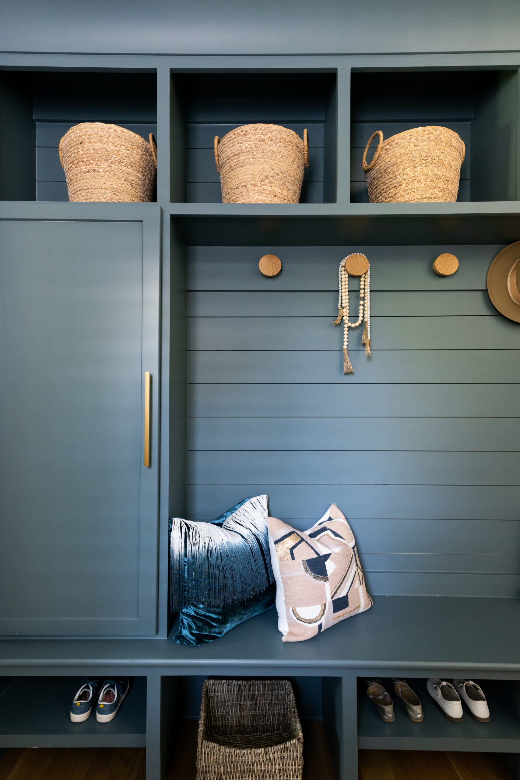 Navy mud bench with gold circular hooks and a bench to sit on, open shelving with basket storage above and open shelving and space below the bench with a locker on one end