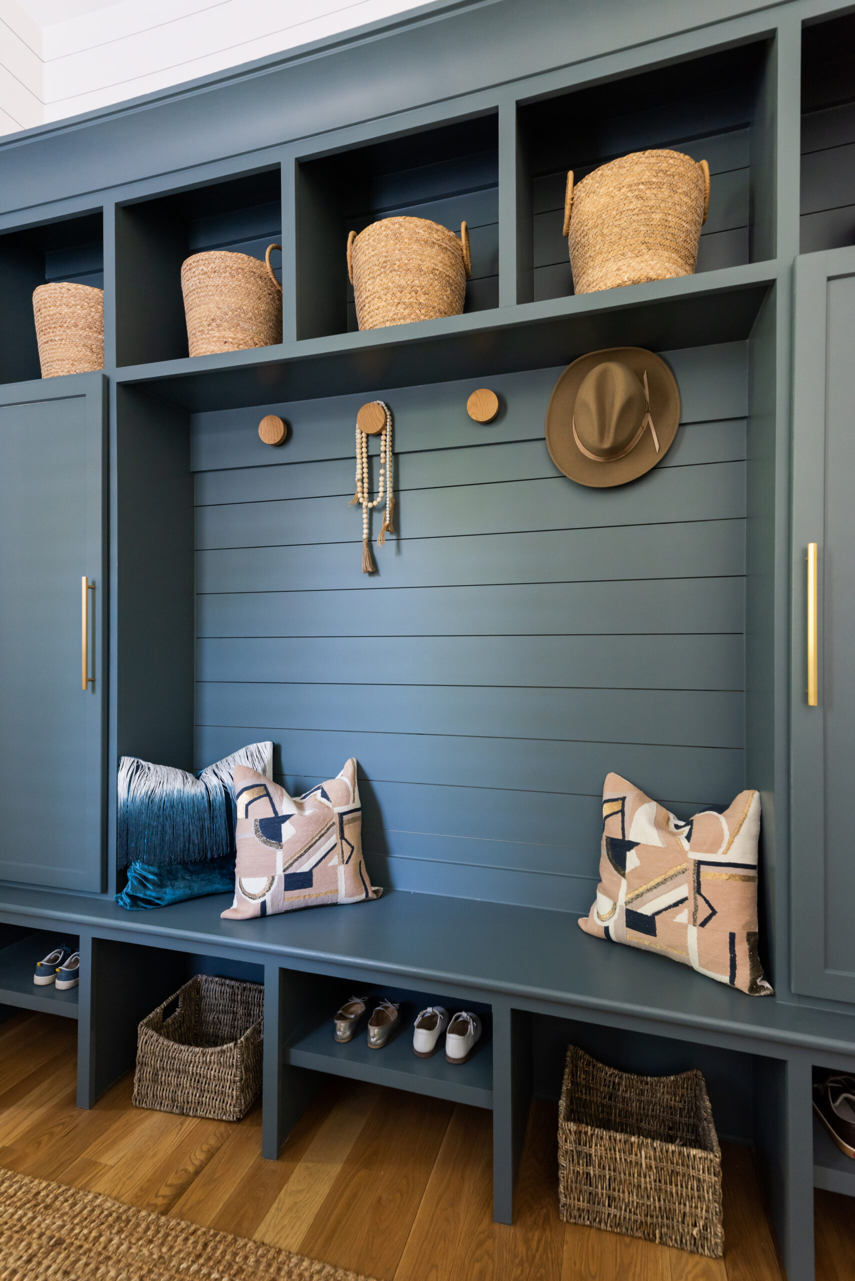 Navy mud bench with gold circular hooks and a bench to sit on, open shelving with basket storage above and open shelving and space below the bench with a locker on one end