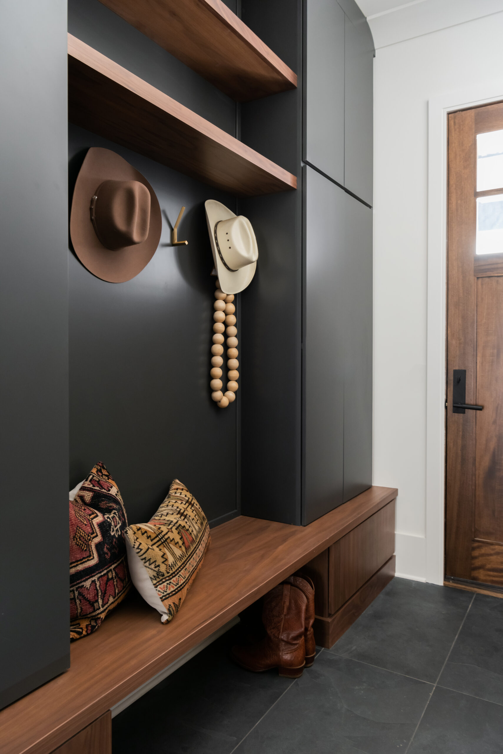 Entryway black mud bench with lockers on each end and hooks and open shelving above and below the bench