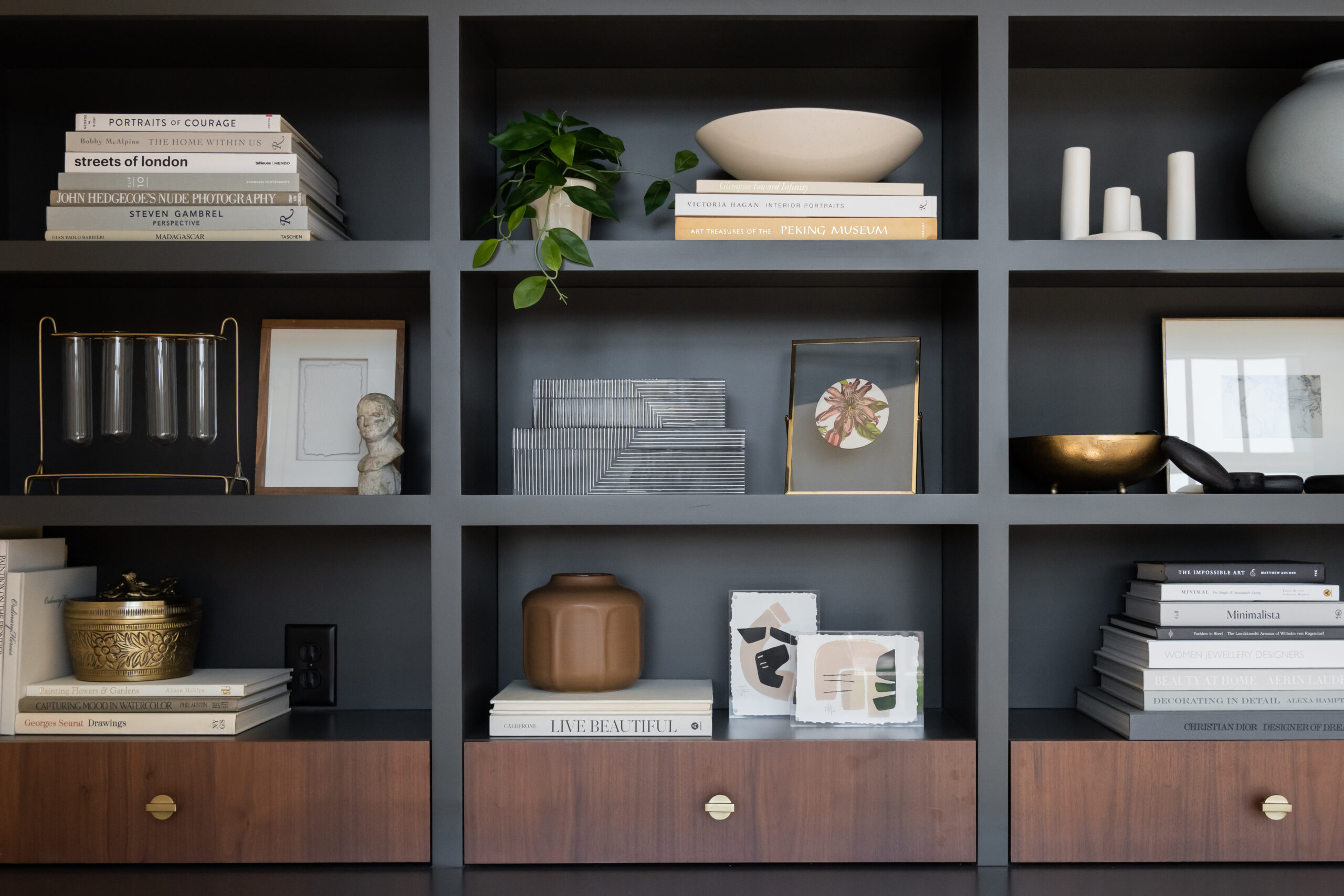 Black bookcase with open shelving and wood paneled drawers at base of upper shelving