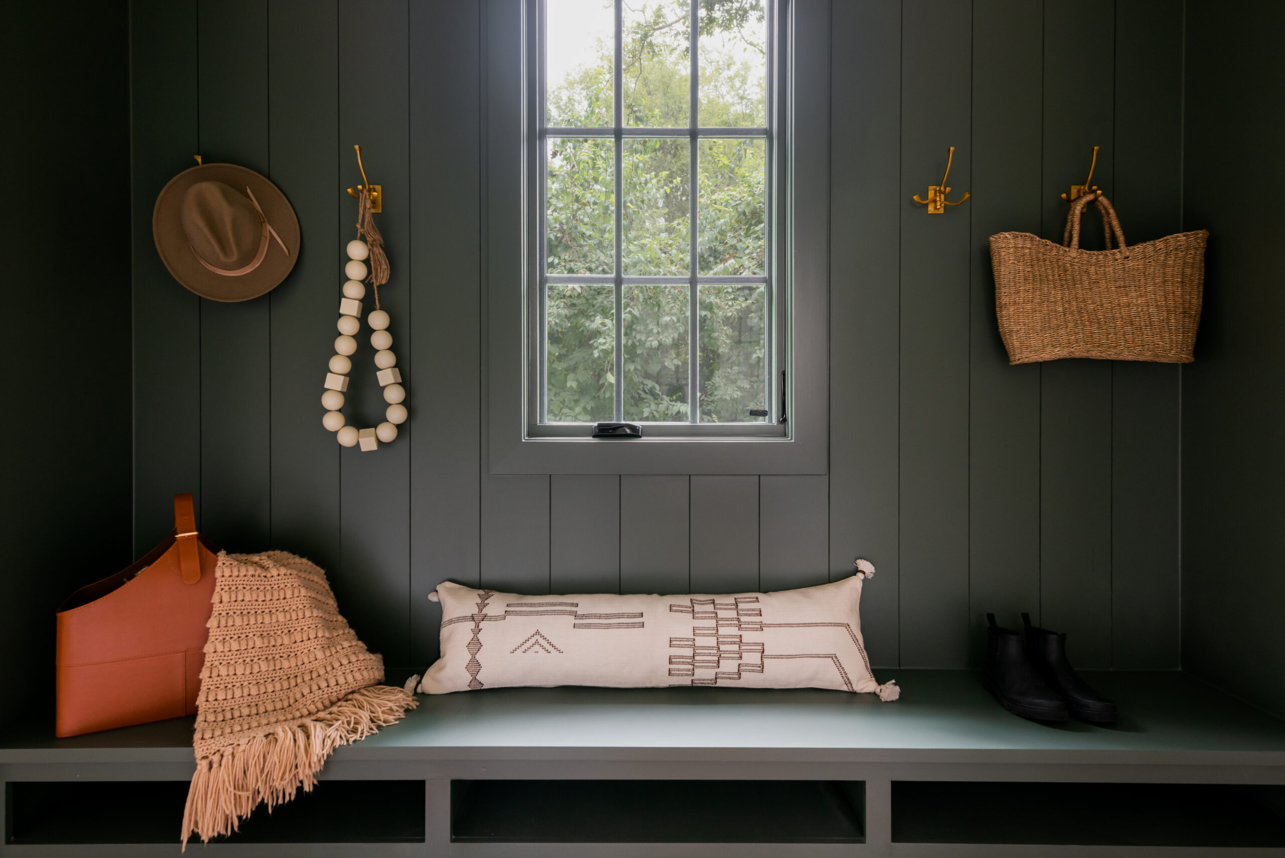 Entryway mudbench with hooks on paneled wall, open shelving below bench and grean painted paneling framing the back wall and window above the bench