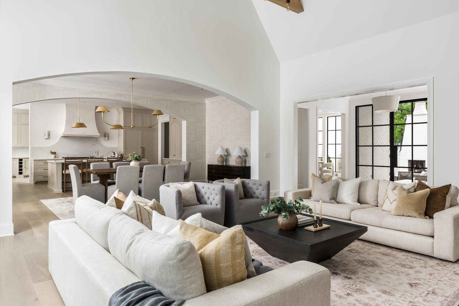 High ceiling family room with wood beams, white walls, taupe stucco fireplace and a wall of black grid windows