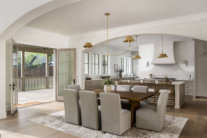 Double arched openings with simple chandelier, dining table with chairs and french doors opening to the back porch