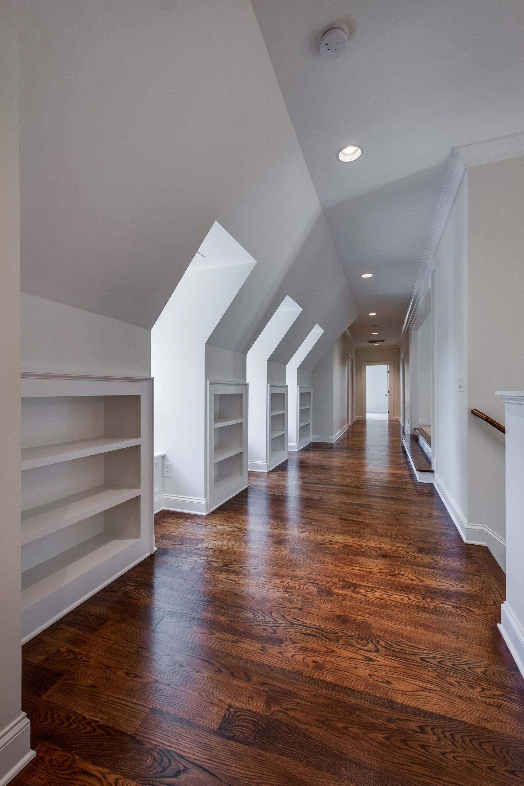 Upstairs hallway with dormers and builtin open, white bookshelves and warm hardwood flooring
